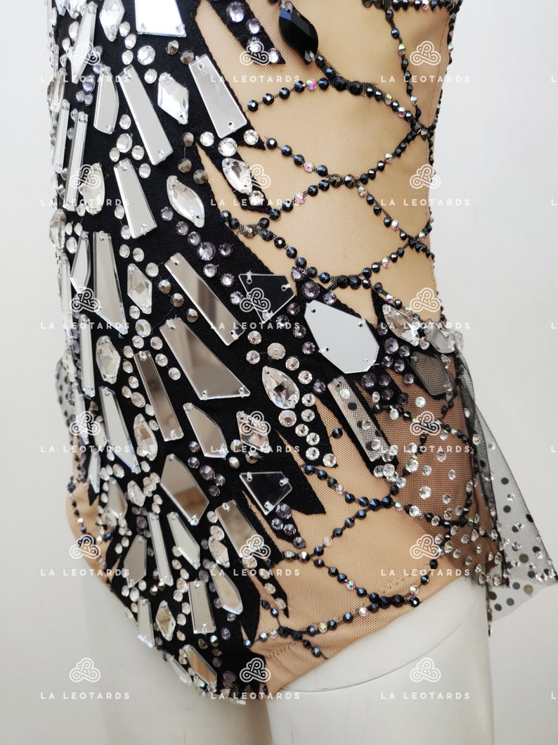 May include: A black leotard with a sheer mesh overlay and a design of silver and black rhinestones. The leotard has a scoop neck and a low back.