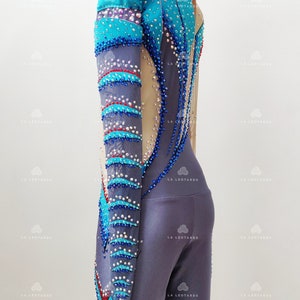 Op de afbeelding: Een langarmige maillot met een blauw, grijs en rood ontwerp. De maillot is bedekt met strass steentjes en heeft een mesh paneel in de rug.