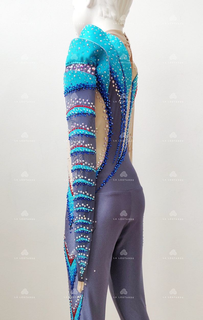 Op de afbeelding: Een langarmige maillot met een blauw, grijs en rood ontwerp. De maillot is bedekt met strass steentjes en heeft een mesh paneel in de rug.