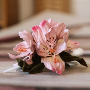 以下が含まれることがあります： 濃いピンク色の先端と濃い斑点が付いた、明るいピンク色の造花のクローズアップ。 花には緑の葉と白い茎があります。 花はおそらくブートニアまたはコサージュです。