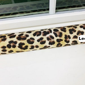 May include: A brown and tan leopard print draft stopper. The draft stopper is made of fabric and has the word "Leopard" printed on it.