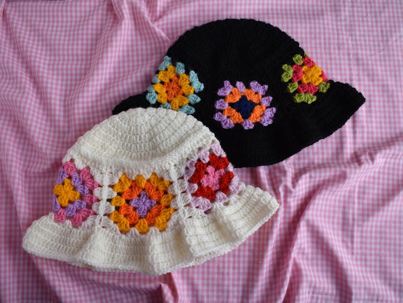 May include: Two crocheted bucket hats, one white with colorful granny squares and one black with purple, blue, and green granny squares.
