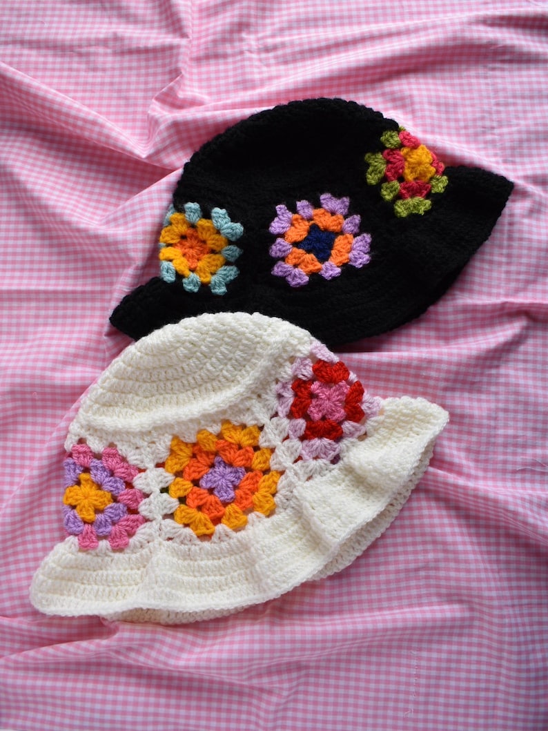 May include: Two crocheted bucket hats with colorful granny square designs. One hat is black with multi-colored squares, and the other is white with pink, orange, and purple squares.