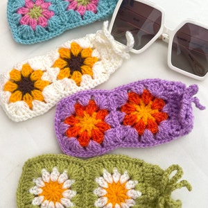 K&ouml;nnte beinhalten: Vier geh&auml;kelte Brillenetuis mit verschiedenen Blumendesigns. Die Etuis sind in Blau, Wei&szlig;, Lila und Gr&uuml;n. Jedes Etui hat ein geh&auml;keltes Blumendesign mit einem anderen Farbschema.