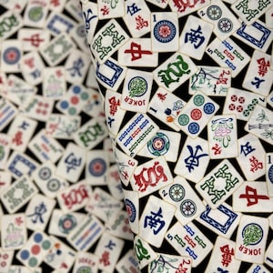 May include: Close-up of fabric featuring a repeating pattern of Mahjong tiles. The tiles are white with red, green, blue, and black symbols and characters. The background is black, creating a high-contrast design.