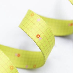 May include: A bright yellow ribbon featuring a thin orange grid pattern across its surface. The ribbon is decorated with small, repeating orange and pink circular icons scattered throughout the grid, creating a consistent graphic design.