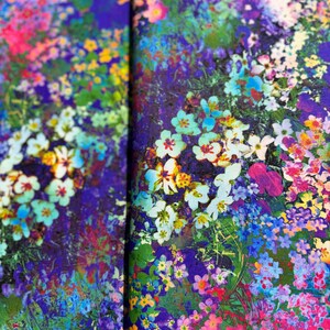 Op de afbeelding: Een levendige bloemenprintstof met een verscheidenheid aan kleurrijke bloemen, waaronder roze, paars, blauw, geel en wit. De stof heeft een textuur, bijna als een aquarel.