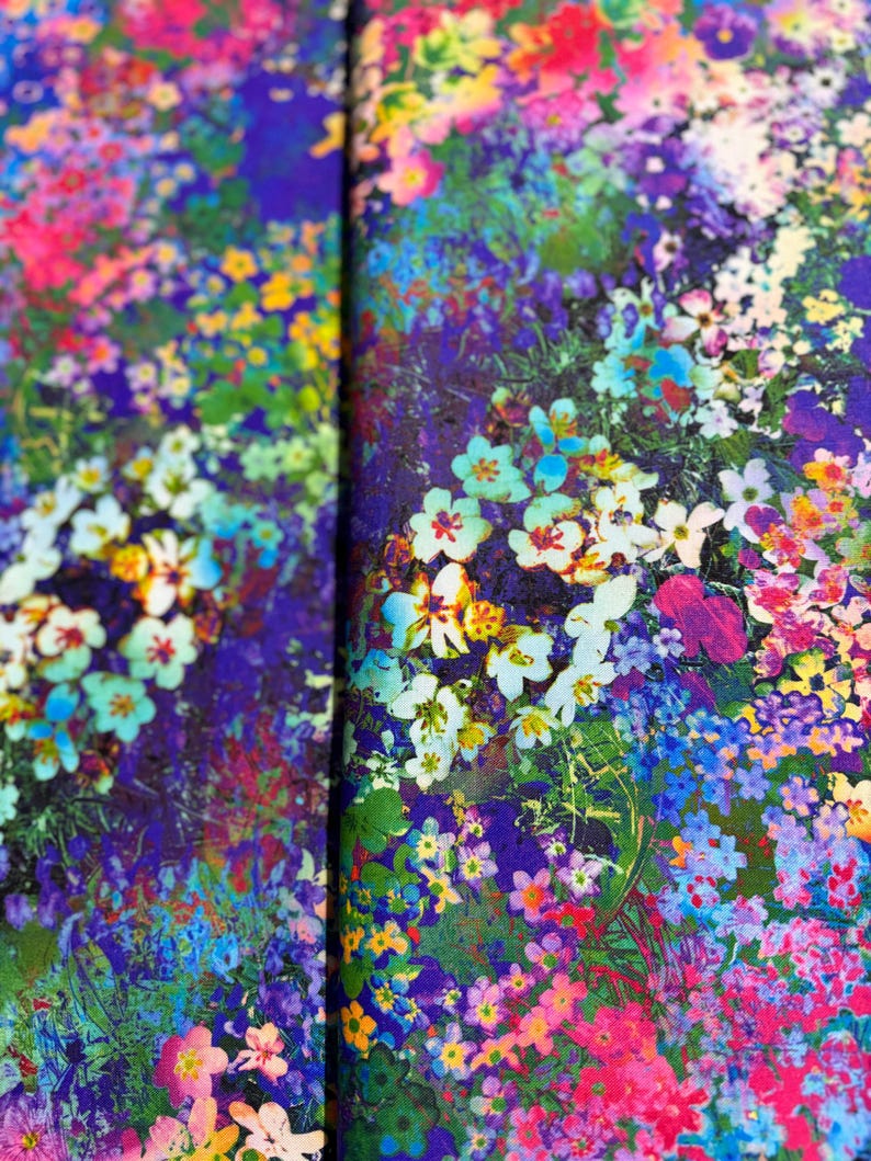 Op de afbeelding: Een levendige bloemenprintstof met een verscheidenheid aan kleurrijke bloemen, waaronder roze, paars, blauw, geel en wit. De stof heeft een textuur, bijna als een aquarel.