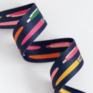 May include: Navy blue ribbon featuring a repeating pattern of colourful, stylised pencils. The pencils are in shades of pink, orange, yellow, and green. The ribbon is curled, displaying the pattern from various angles.