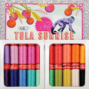 May include: A box of 24 spools of Aurifil thread in a rainbow of colors. The box has a Tula Pink design with a monkey and cherries. The text on the box reads "Tula Pink" and "Tula Sunrise".