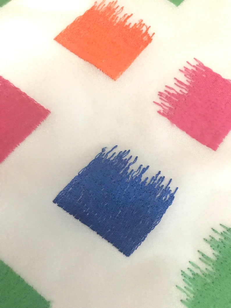 May include: A white fabric with embroidered squares in various colours, including orange, pink, blue, and green. The squares are filled with a textured, brushstroke-like pattern.