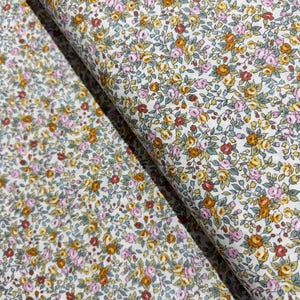 Könnte beinhalten: Weißer Stoff mit einem kleinen floralen Druck mit rosa, gelben und orangefarbenen Blumen. Der Stoff ist in der Mitte gefaltet und zeigt das Muster auf beiden Seiten.