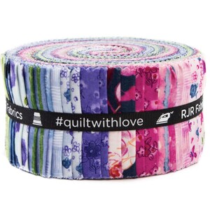 May include: A jelly roll of fabric strips featuring a variety of floral and geometric patterns in shades of pink, purple, blue, and green. A black ribbon wraps around the center with the text RJR Fabrics, #quiltwithlove, and icons of a thimble and iron.