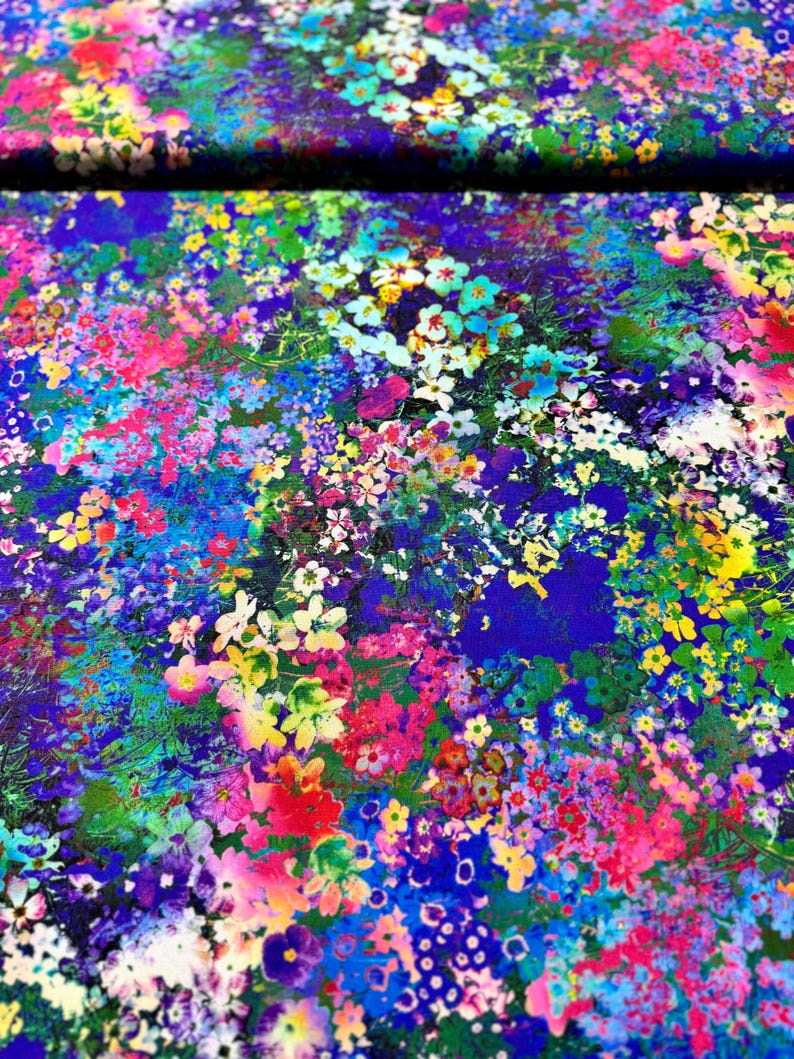 Op de afbeelding: Een levendige bloemenprintstof met een blauwe achtergrond. De stof is bedekt met een verscheidenheid aan kleurrijke bloemen, waaronder roze, gele, witte en blauwe.