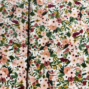 May include: White fabric with a floral pattern featuring pink, red, and green flowers. The fabric has a subtle texture and a delicate design.