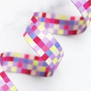 May include: Close-up of a patterned ribbon. The ribbon has a checkered design with squares of pink, red, purple, yellow, and blue. The ribbon is curled and made of fabric.