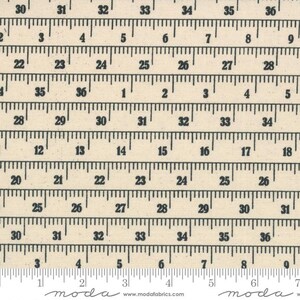 May include: A beige fabric with a repeating pattern of black ruler markings. The ruler markings show inches from 30 to 36. The fabric has the words "moda" and "www.modafabrics.com" printed on the bottom.