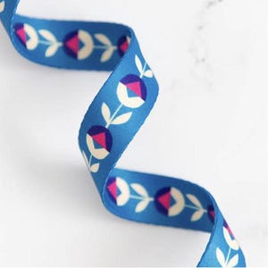 May include: A blue ribbon featuring a repeating floral design. The flowers are white, pink, and purple, with green leaves. The ribbon is curved and likely made of fabric.