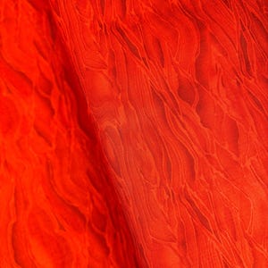 Peut inclure: Tissu rouge avec un motif marbré. Le tissu a une texture lisse et soyeuse.