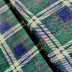 Op de afbeelding: Close-up van een groene, witte, blauwe en roze geruite stof. De stof heeft een zachte, pluche textuur.