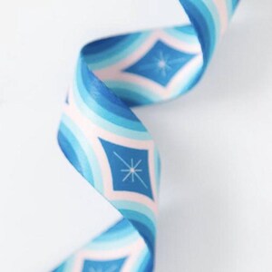 May include: A decorative ribbon in shades of blue, light blue, and pink, with a repeating diamond and starburst pattern. The ribbon is curled, suggesting it's made of fabric. The design has a retro aesthetic, suitable for crafts or gift wrapping.