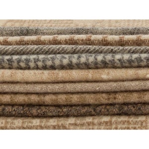 Puede incluir: Primer plano de una pila de muestras de tela en tonos neutros. Las telas muestran una variedad de texturas y patrones, incluyendo espiga y diseños geométricos. La paleta de colores incluye beige, marrón y gris, destacando la variedad de los textiles.