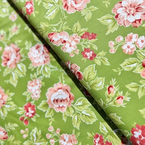 May include: Close-up of green fabric with a floral pattern. The design features large pink and white roses, smaller red flowers, and green leaves. The fabric is folded, showing the pattern's repeat.