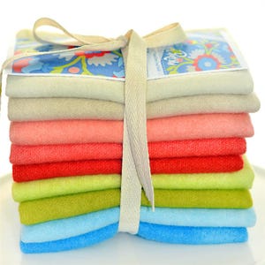Op de afbeelding: Een stapel van tien stofvierkanten in verschillende tinten roze, rood, groen en blauw, gebonden met een wit lint. De stofvierkanten zijn gerangschikt in een regenboogpatroon, met de lichtste tint bovenaan en de donkerste tint onderaan.