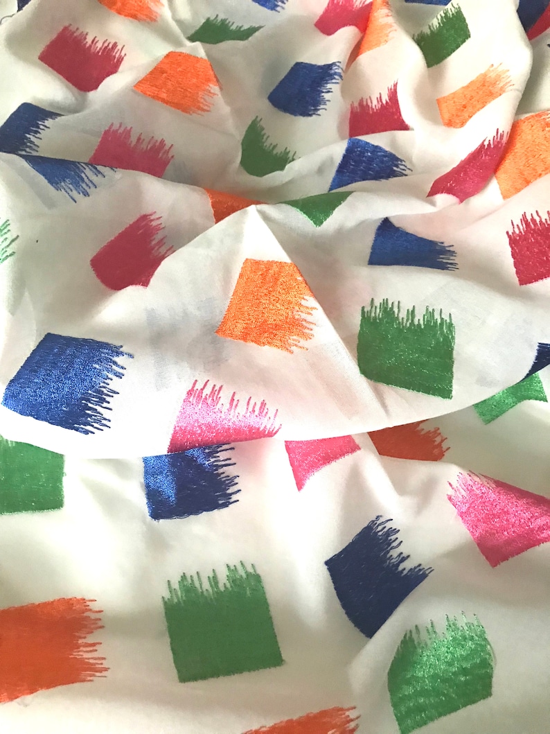 May include: White fabric with a repeating pattern of colourful embroidered squares. The squares are in shades of blue, green, pink, and orange.