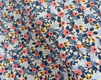 May include: A white fabric with a repeating pattern of pink and blue flowers on a navy blue background. The fabric is folded in half, showing the pattern on both sides.