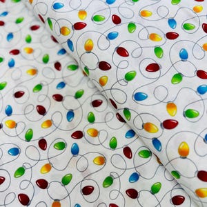 Puede incluir: Tela blanca con un patrón repetido de luces navideñas coloridas. Las luces son rojas, verdes, azules y amarillas, conectadas por líneas grises onduladas. La tela está doblada, mostrando el patrón desde diferentes ángulos.