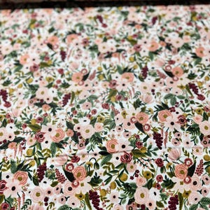May include: A white fabric with a floral pattern featuring pink, red, and green flowers. The fabric is covered in a dense pattern of flowers and leaves.