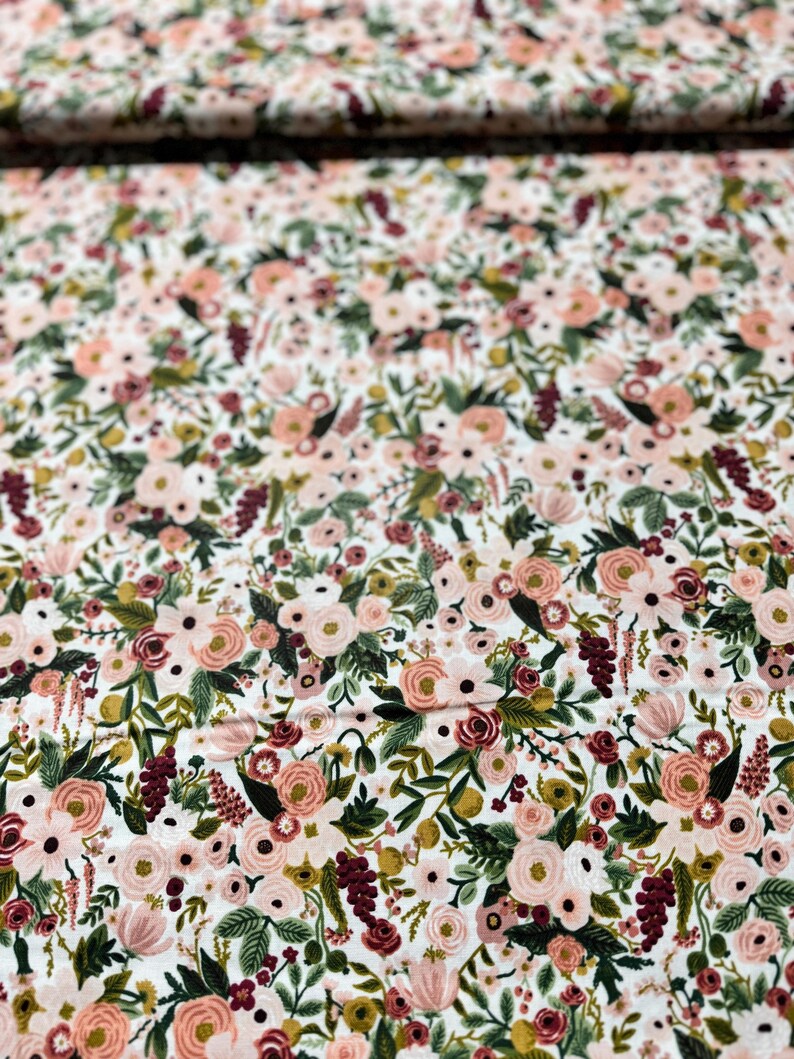 May include: A white fabric with a floral pattern featuring pink, red, and green flowers. The fabric is covered in a dense pattern of flowers and leaves.