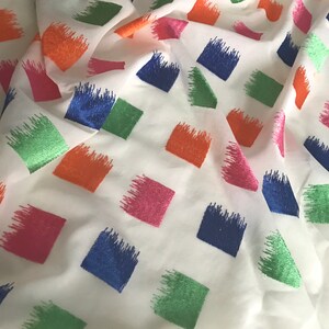 May include: White fabric with a repeating pattern of colourful squares. The squares are outlined in a brushstroke style and are in shades of blue, green, pink, and orange.