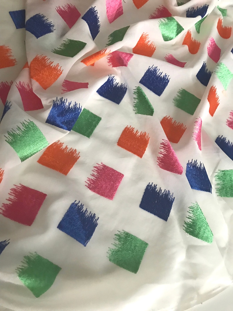 May include: White fabric with a repeating pattern of colourful squares. The squares are outlined in a brushstroke style and are in shades of blue, green, pink, and orange.
