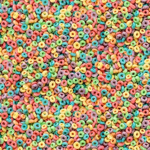 May include: A close-up image of a colourful cereal with a variety of colours, including red, orange, yellow, green, blue, and purple. The cereal is shaped like small rings.