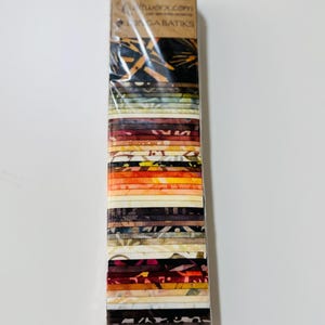 Puede incluir: Un paquete de 42 cuadrados de tela de tamaño "fat quarter" en una variedad de colores cálidos marrones, naranjas y crema con diferentes patrones. La tela está etiquetada como "Timeless Treasures" y "Tonga Batiks".