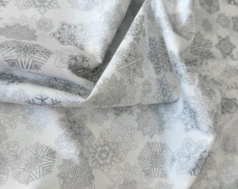 Può includere: Tessuto bianco con un motivo ripetitivo di fiocchi di neve grigi. Il tessuto è piegato a metà e il motivo è visibile su entrambi i lati.