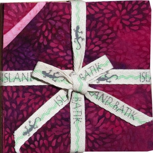 May include: A bundle of five fat quarters of fabric in a deep red and purple batik print with a white and green ribbon tied around it. The ribbon has the words "Island Batik" printed on it.