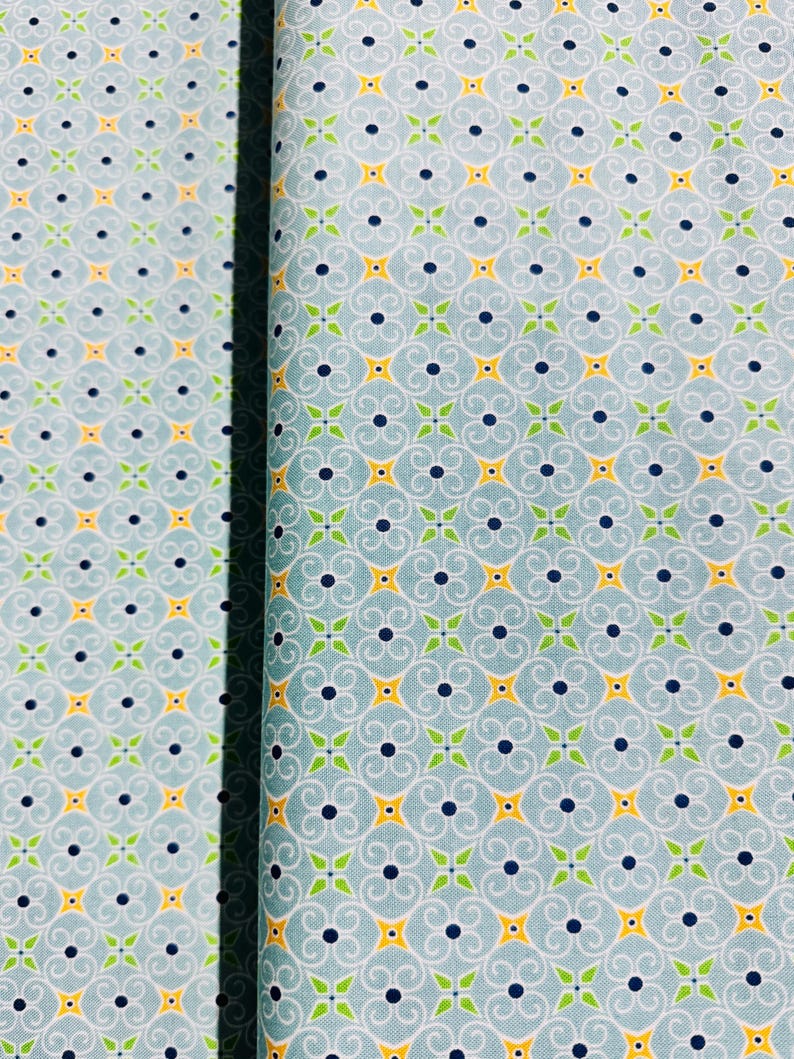May include: A blue fabric with a repeating pattern of yellow stars, green leaves, and black dots. The pattern is a stylized floral design.