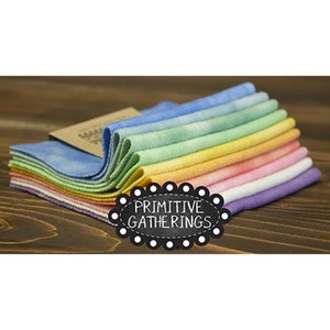 Op de afbeelding: Een stapel van tien regenboog tie-dye stof vierkanten met de tekst "PRIMITIVE GATHERINGS" op een zwart label.