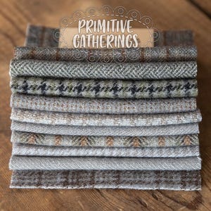 Puede incluir: Una pila de diez cuadrados de tela en varios tonos de gris y marrón con un sutil patrón de cuadros. Los cuadrados de tela están dispuestos en una pila ordenada y tienen una apariencia suave y texturizada. El texto "PRIMITIVE GATHERINGS" es visible en una etiqueta en el centro superior de la imagen.