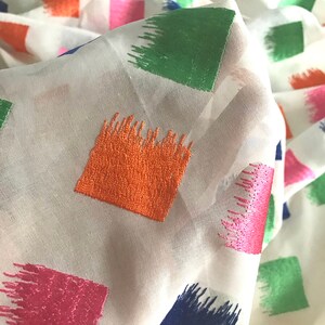 May include: White fabric with a geometric pattern of colourful squares. The squares are embroidered with a brushstroke design in shades of pink, orange, green, and blue.
