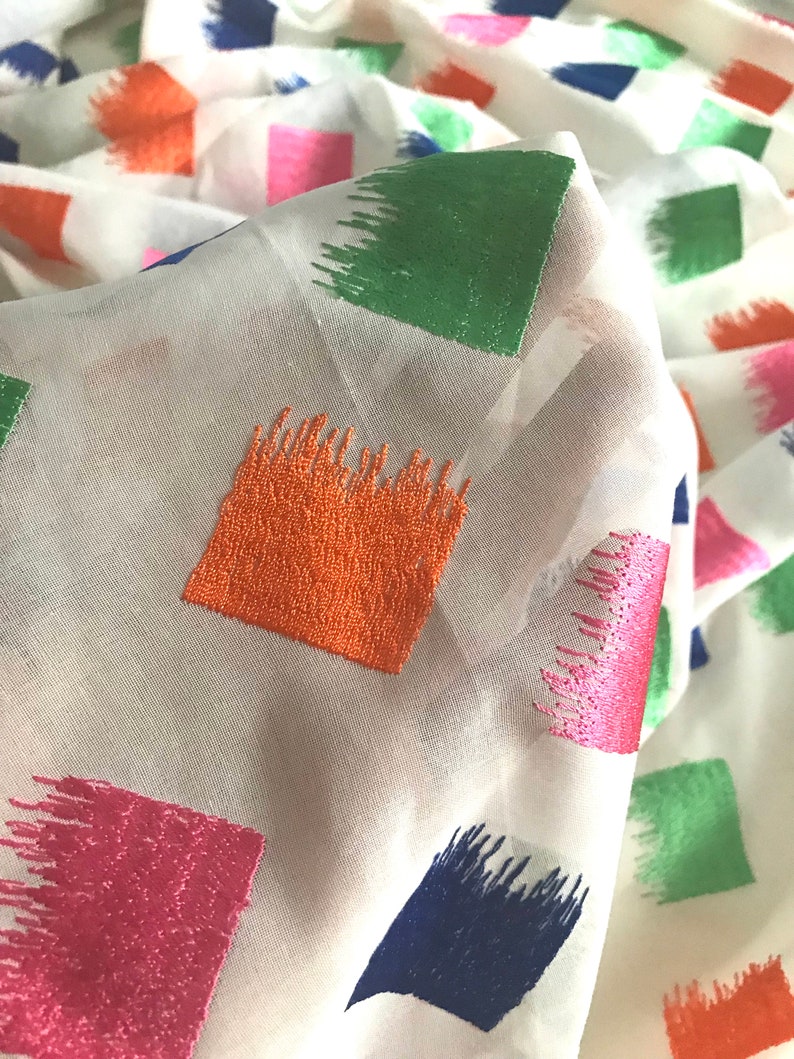 May include: White fabric with a geometric pattern of colourful squares. The squares are embroidered with a brushstroke design in shades of pink, orange, green, and blue.