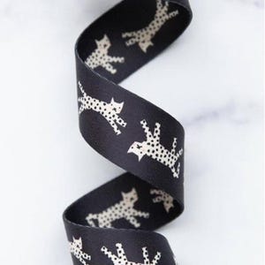 May include: Black ribbon featuring a repeating pattern of white dotted cat silhouettes. The ribbon is curled, displaying the design. Suitable for crafts, gift wrapping, or other creative projects.