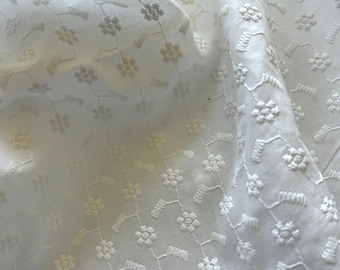 May include: White cotton fabric with a delicate floral embroidery pattern. The fabric is lightweight and has a soft texture.