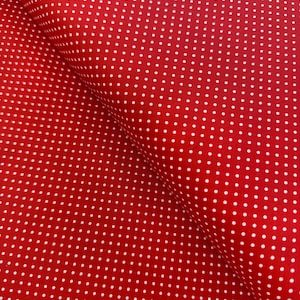 May include: Close-up of red fabric with a pattern of small, evenly spaced white polka dots. The fabric is folded, creating shadows and highlighting the texture. The polka dot pattern is a classic design element.