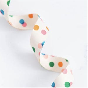 May include: A cream-coloured ribbon with a repeating pattern of colourful polka dots in blue, green, orange, and pink. The ribbon is curled and appears to be made of fabric.