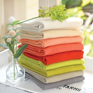 May include: A stack of eight fabric swatches in various colors, including white, cream, peach, orange, red, lime green, yellow, and gray. The swatches are folded neatly and arranged in a pile.