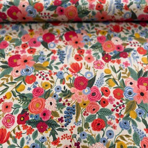May include: A white fabric with a floral pattern featuring pink, red, blue, and green flowers. The fabric is folded in half, showing the pattern on both sides.